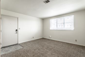 A room with a carpeted floor, a white door, and a window with blinds.